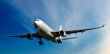 A large commercial airplane with its landing gear down is flying against a clear blue sky, seen from below.