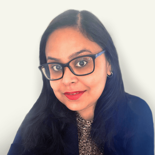 A woman with long black hair, wearing dark-rimmed glasses, a patterned top, and a dark jacket, smiles at the camera against a plain light background—exuding professionalism and confidence in meeting compliance requirements.