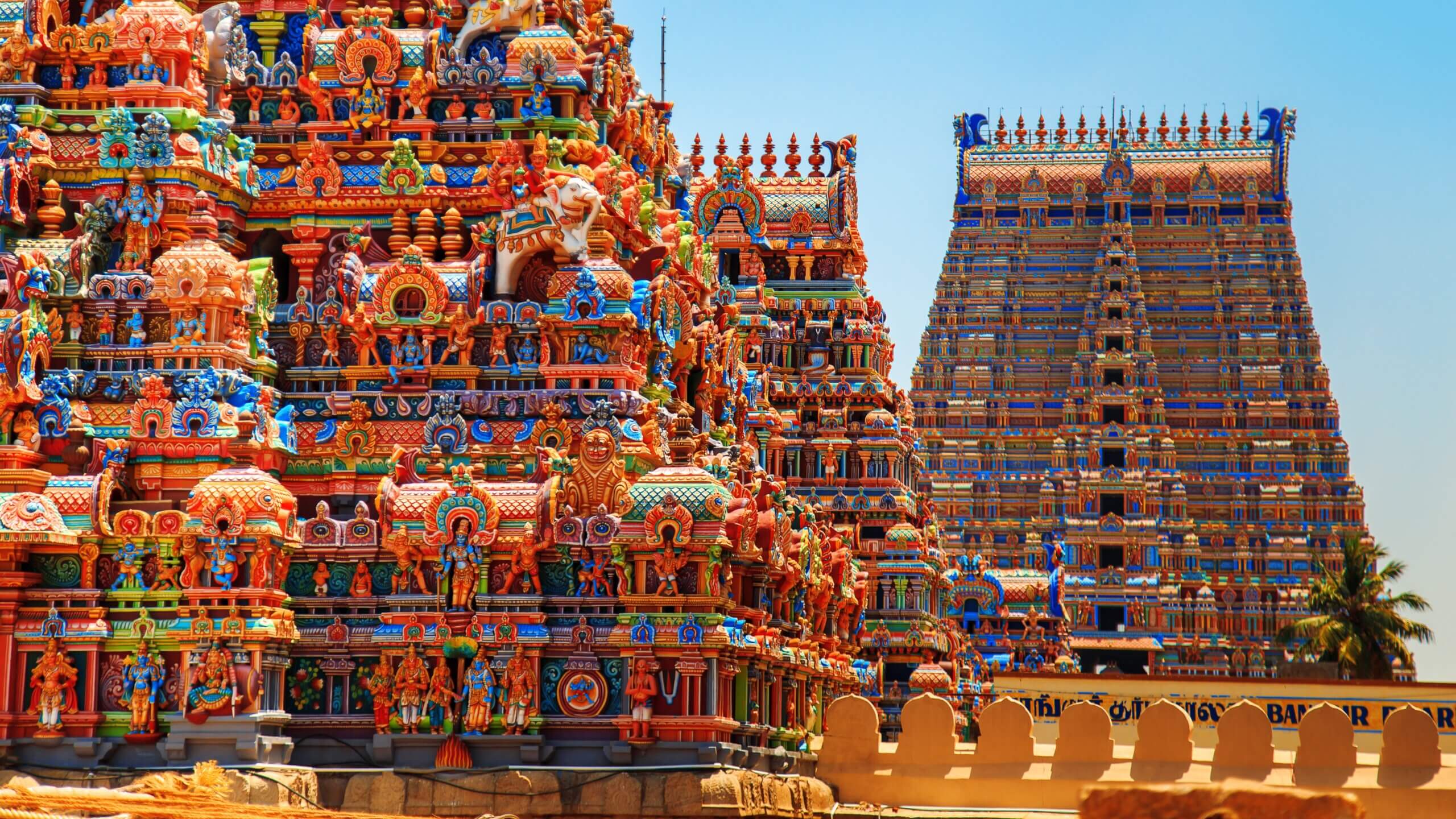 Colorful, intricately decorated towers of a South Indian Hindu temple with detailed sculptures, vibrant carvings, and ornate patterns under a clear blue sky.