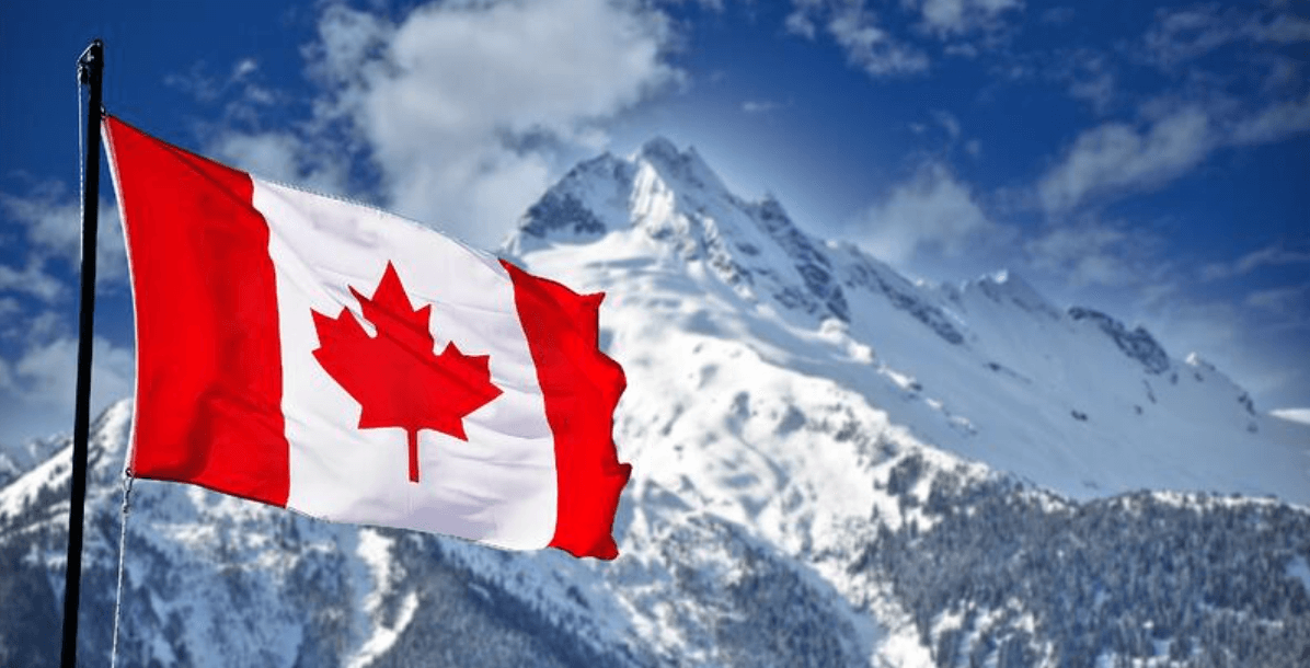 A Canadian flag with a red maple leaf waves in the foreground, with snow-covered mountains and a partly cloudy blue sky in the background.