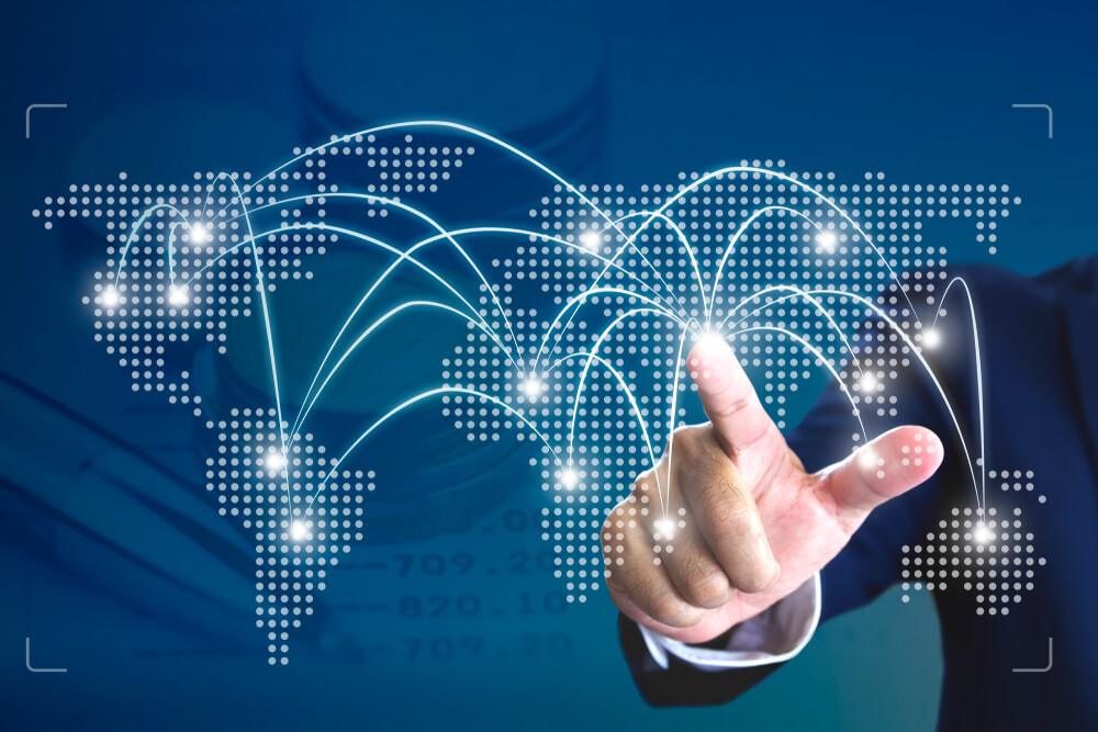 A person in a suit touches a virtual world map with glowing connection lines and nodes, symbolizing global networking or digital communication.